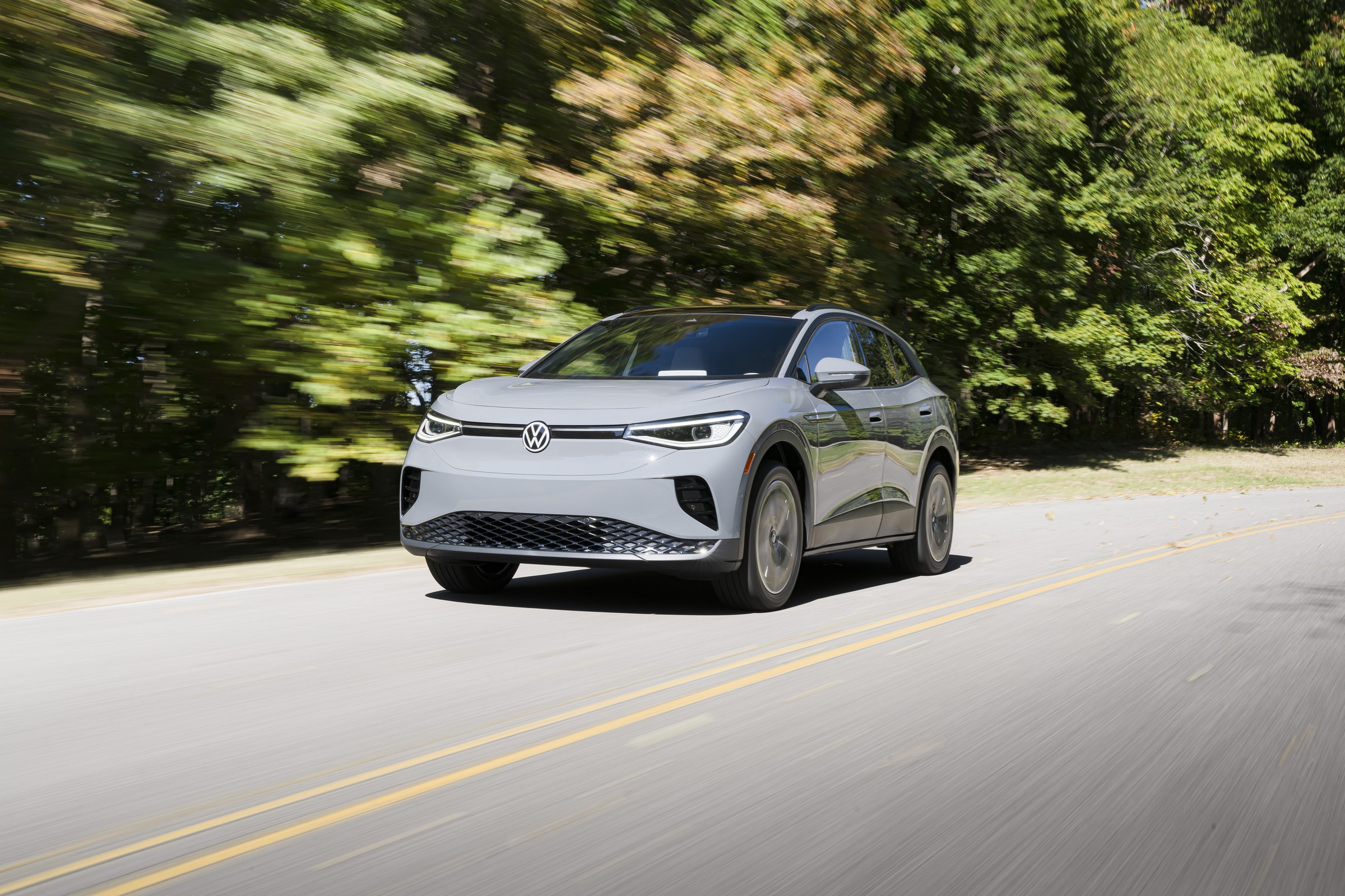 2023 Volkswagen ID.4 electric SUV in silver driving on a tree-lined two-lane road, front three-quarter view; the 2023 model year is the first covered by battery fire recall 26V630