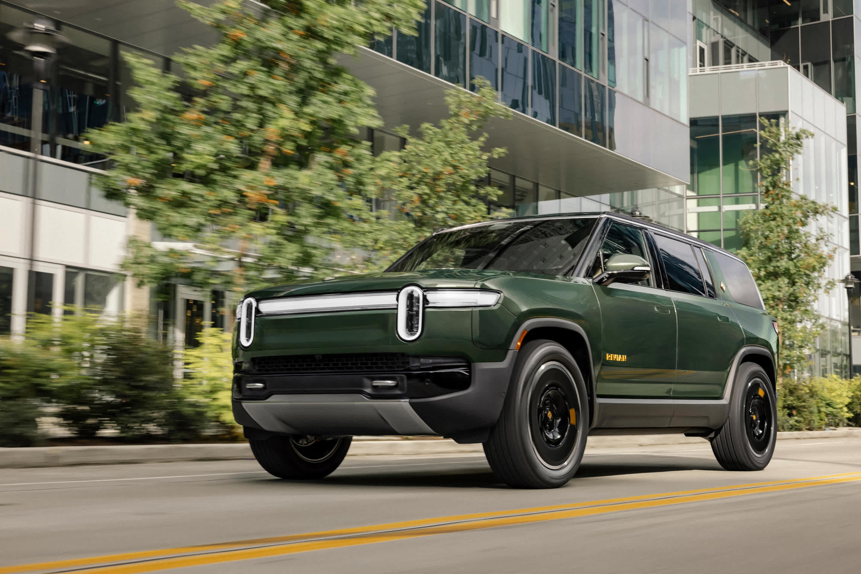 Rivian R1S second-generation three-row electric SUV in green, front three-quarter driving view, the largest model group in recall 26V597000 over an on-screen notification that can block the rearview camera image