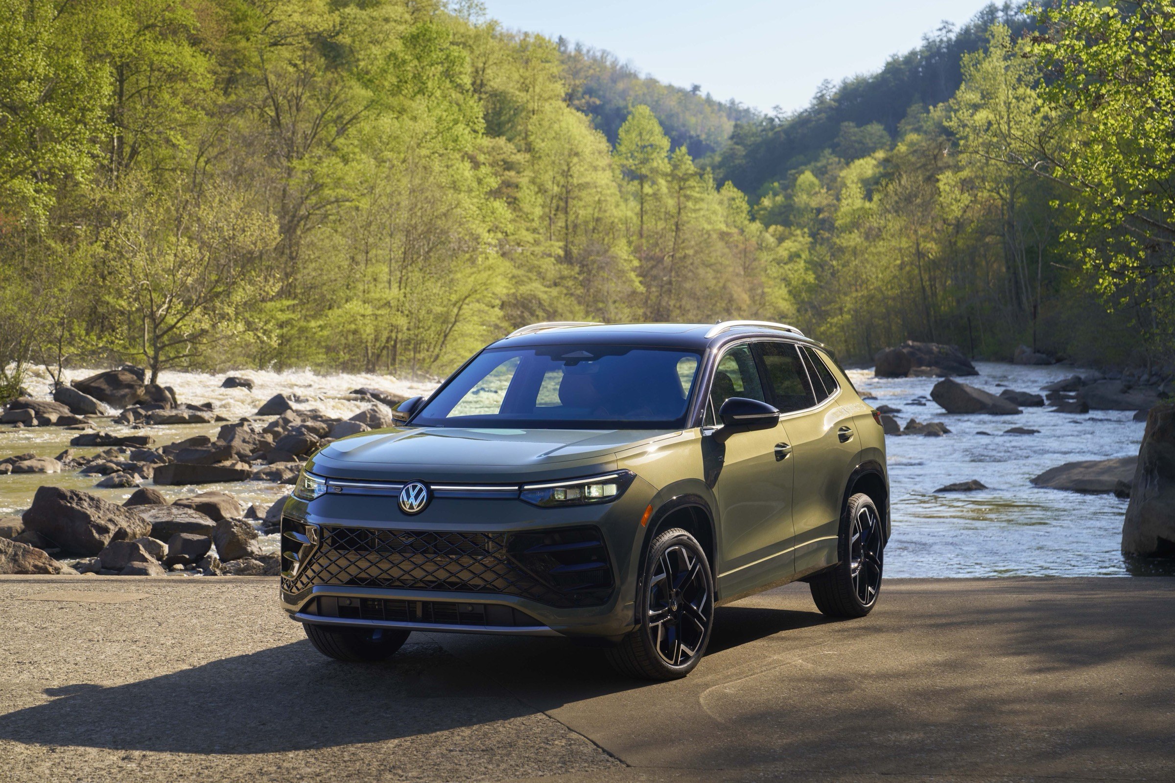 2025 Volkswagen Tiguan SEL R-Line in Avocado Green, front three-quarter view by a river, the third-generation compact SUV recalled under campaign 26V587000 over body control module software that can reset and stall the engine