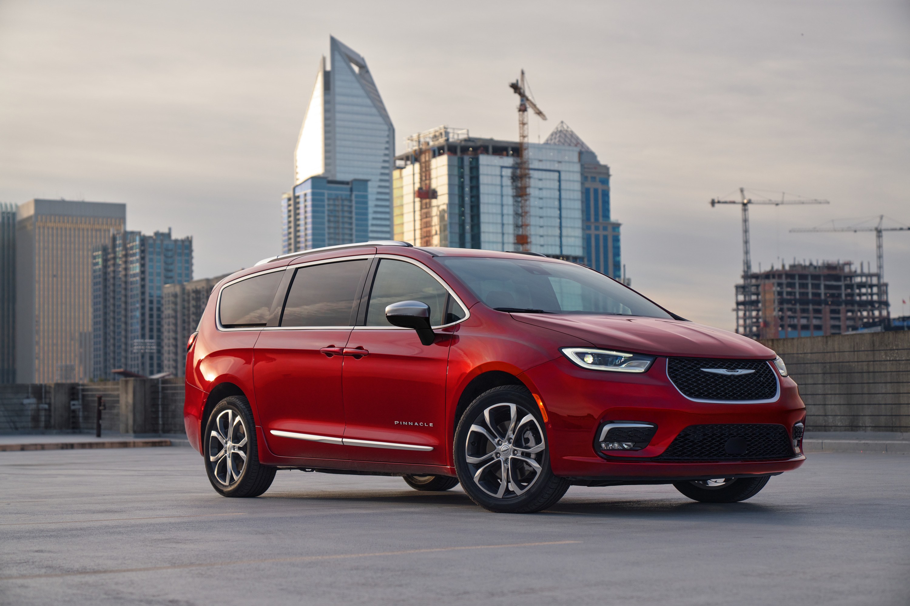 2026 Chrysler Pacifica Pinnacle in Red Hot, front three-quarter view with a city skyline behind, one of the minivans in recall 26V561