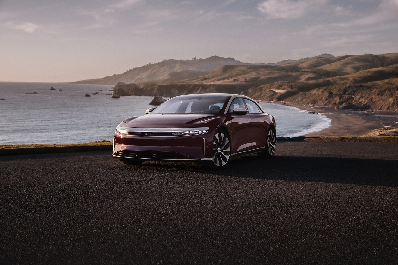 Lucid Air Grand Touring in dark red, front three-quarter view showing the full-width front light blade at the center of recall 26V540