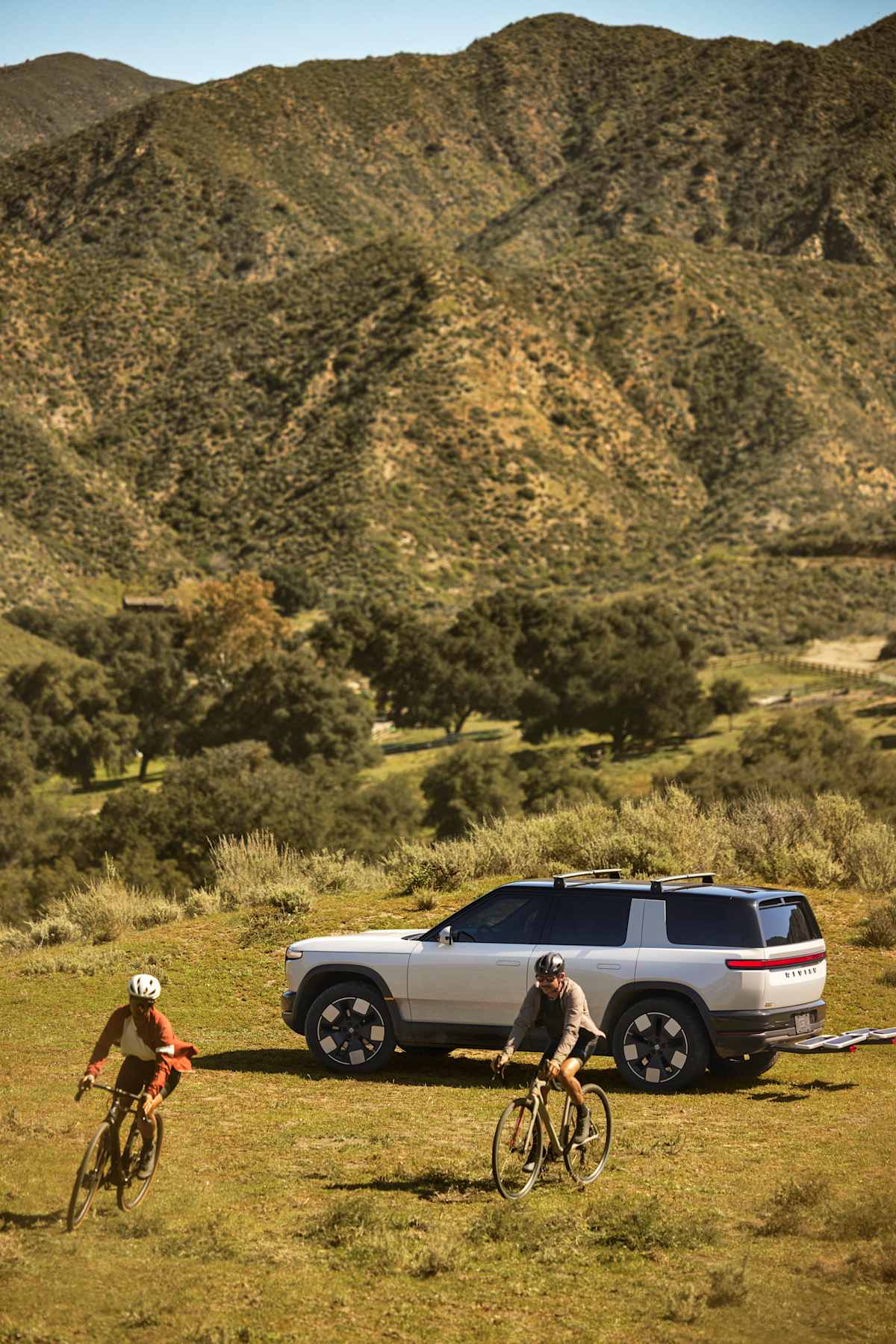 Rivian's 2026 Lineup: Every Model, Every Price, and Which One to Buy 3 2026 Rivian R2 rear three-quarter view with cyclists in mountain landscape