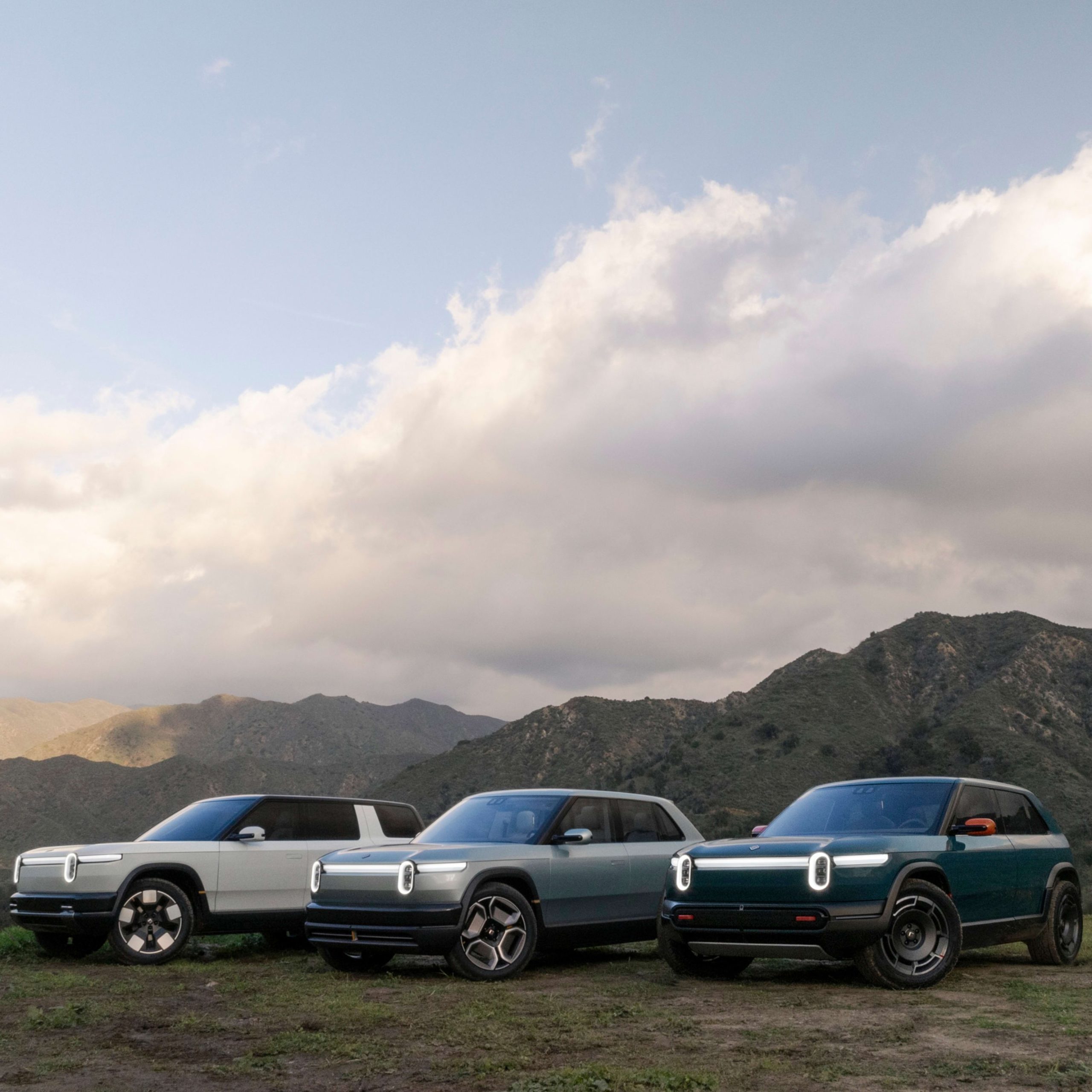 Rivian 2026 lineup with R1T, R2, and R3 electric vehicles parked in a mountain valley at sunset