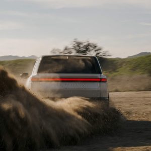 2026 Rivian R2 electric SUV rear view kicking up dirt on a desert trail at golden hour