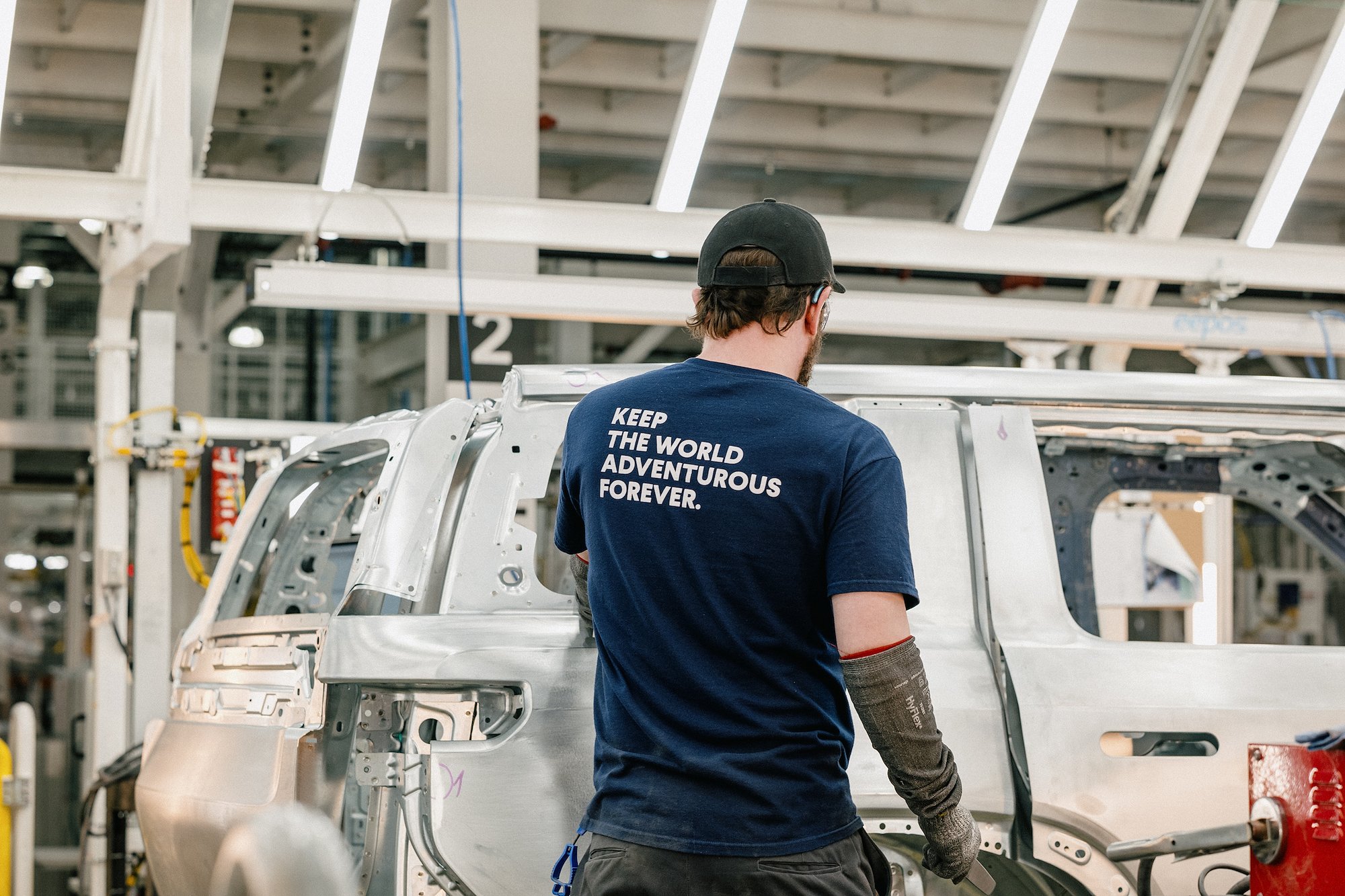 Rivian worker in Keep The World Adventurous Forever shirt assembles R2 body panel on production line