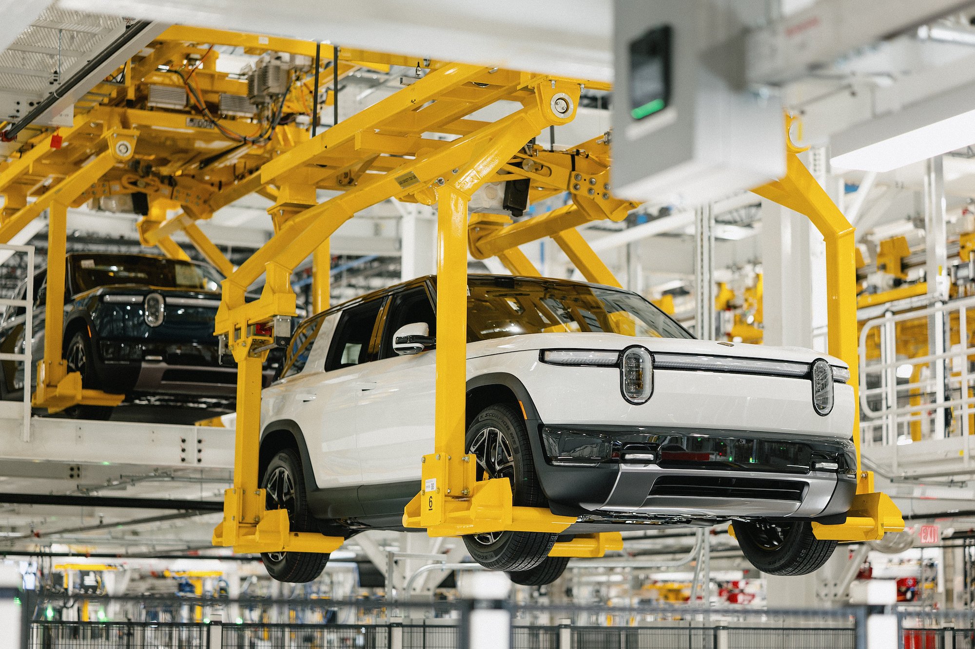 White Rivian R2 body on yellow overhead conveyor system inside Normal Illinois production line