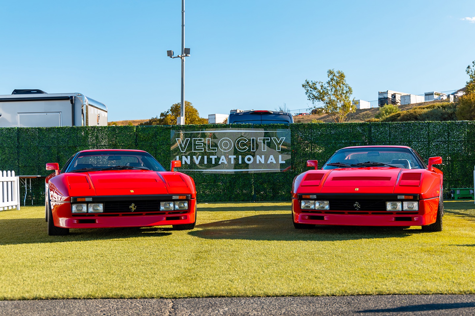 Two red Ferrari 288 GTOs parked in front of the Velocity Invitational signage at Sonoma Raceway