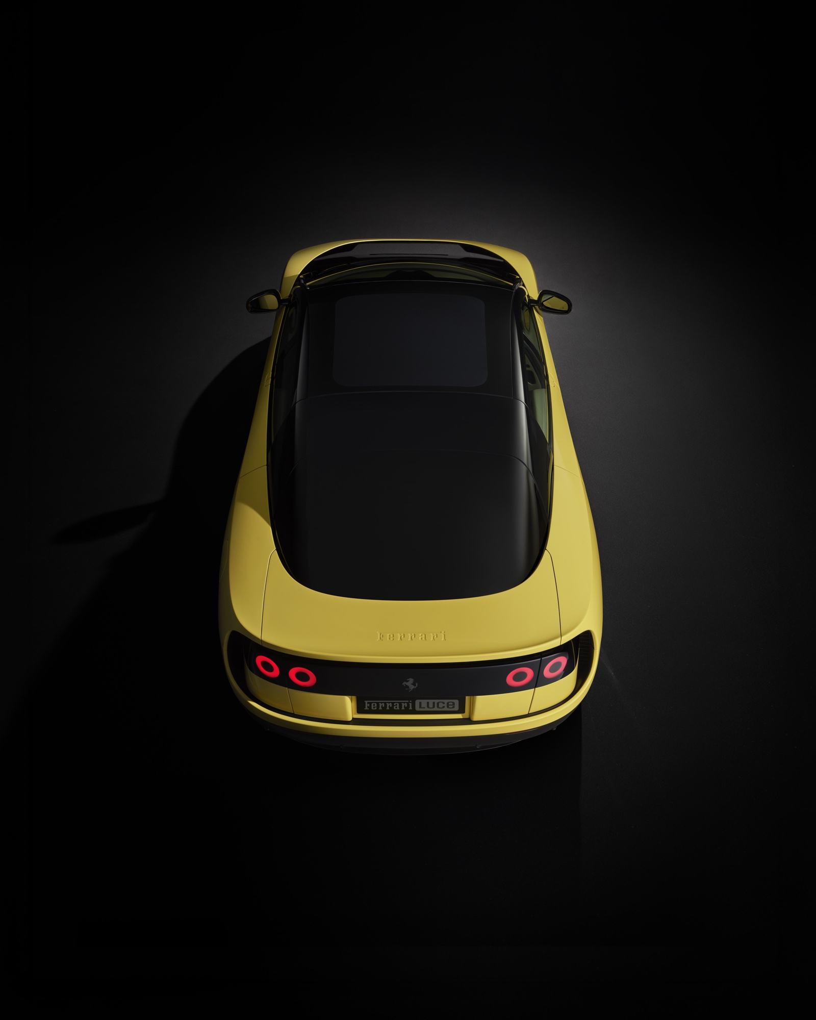 2026 Ferrari Luce top-down view in Giallo Luce yellow against a black studio background with halo tail lights and front headlights illuminated