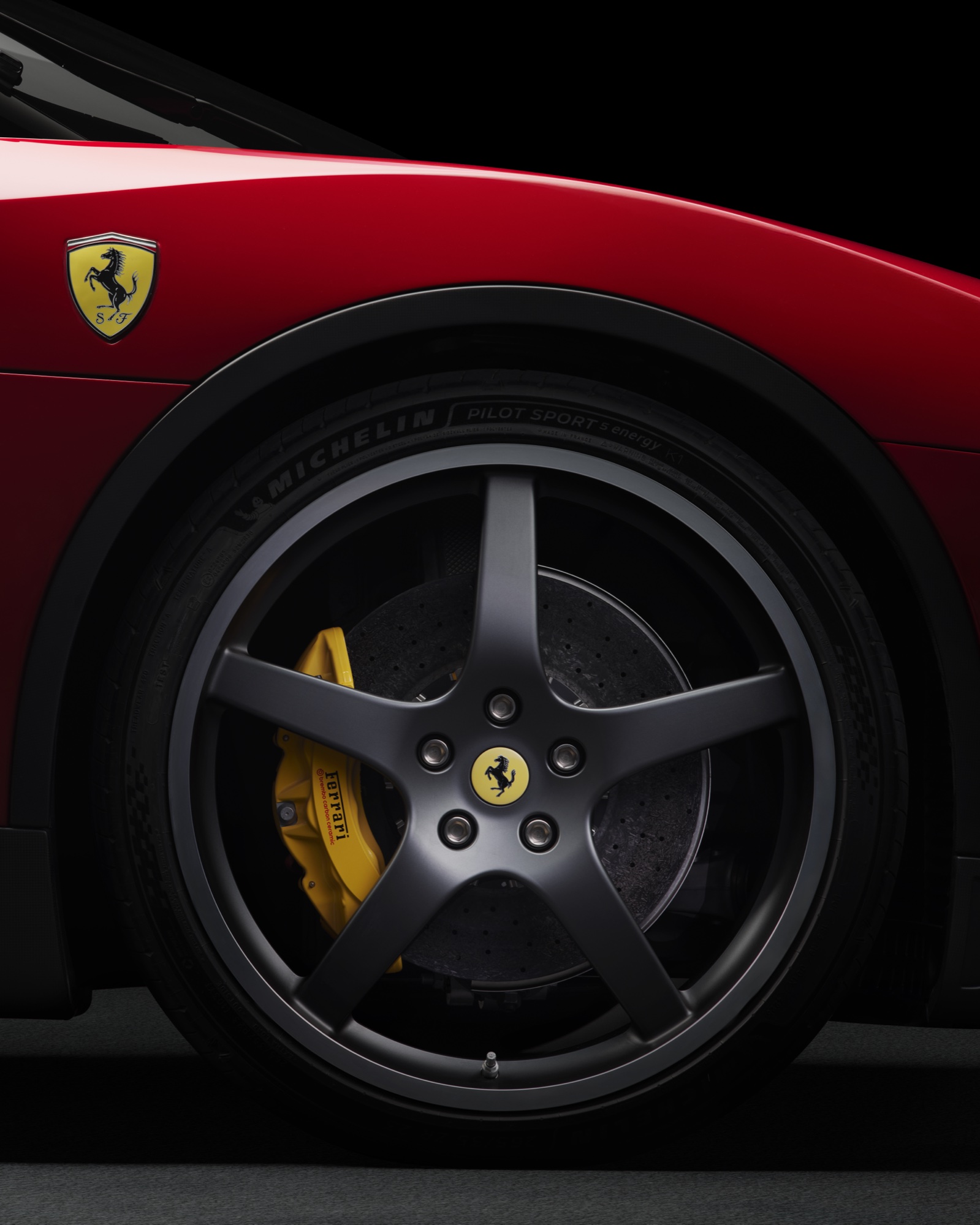 2026 Ferrari Luce wheel detail in Rosso Fiammante showing the 23-inch front wheel with Michelin Pilot Sport tire and yellow Ferrari brake caliper