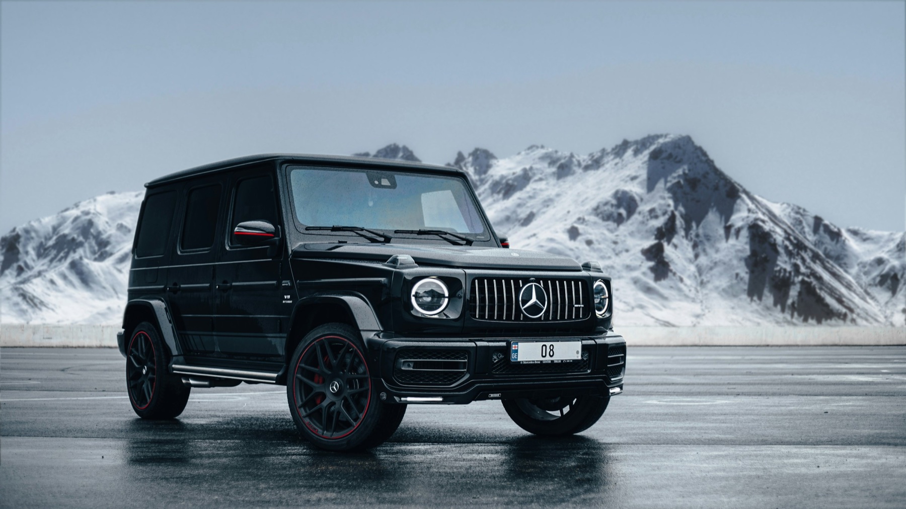 Mercedes-AMG G63 in black with red brake calipers parked against a snowy mountain backdrop, the V8-powered AMG flagship that retained the 4.0-liter biturbo when the G550 moved to inline-six