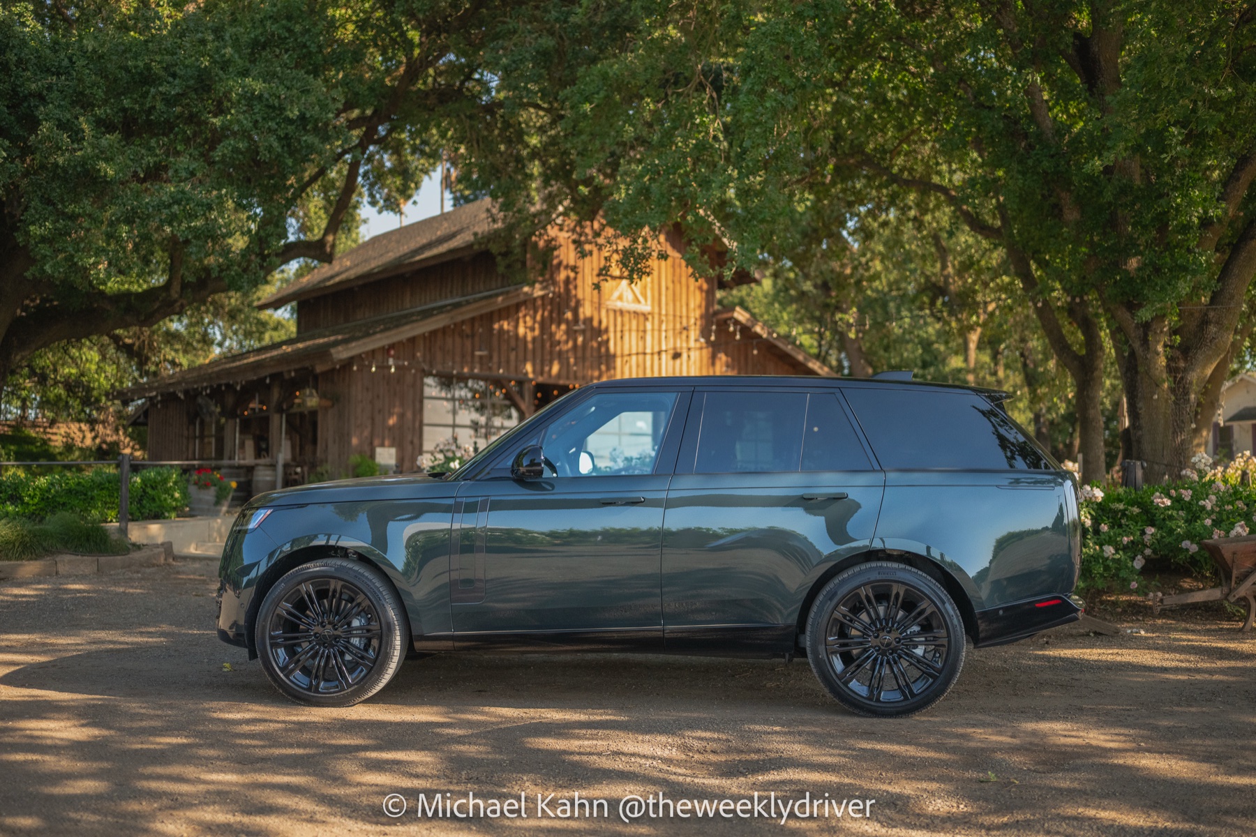 2026 Range Rover SE in Belgravia Green parked side-on under an oak canopy in front of a weathered wooden barn at golden hour