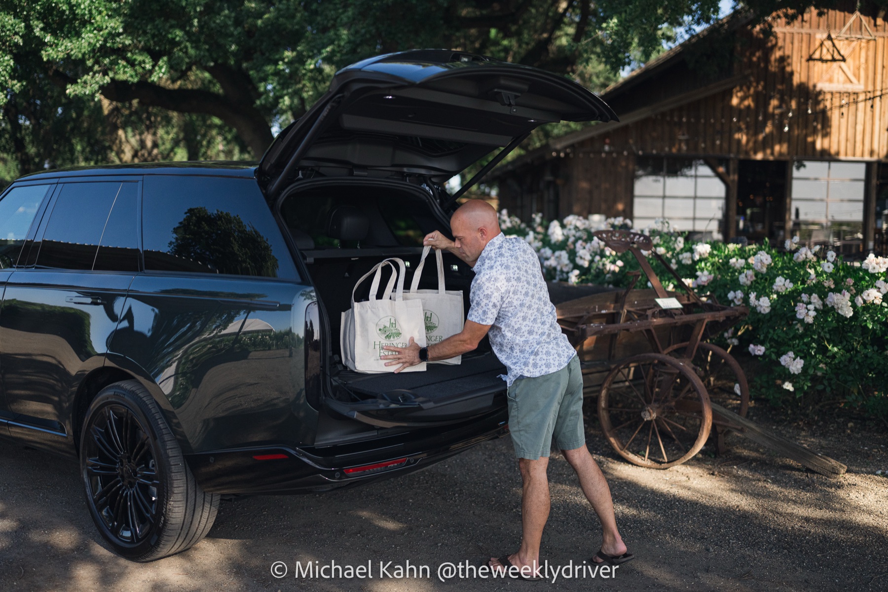 Driver loading two Heringer Estate wine tote bags into the open tailgate of the 2026 Range Rover SE SWB in Belgravia Green at a winery