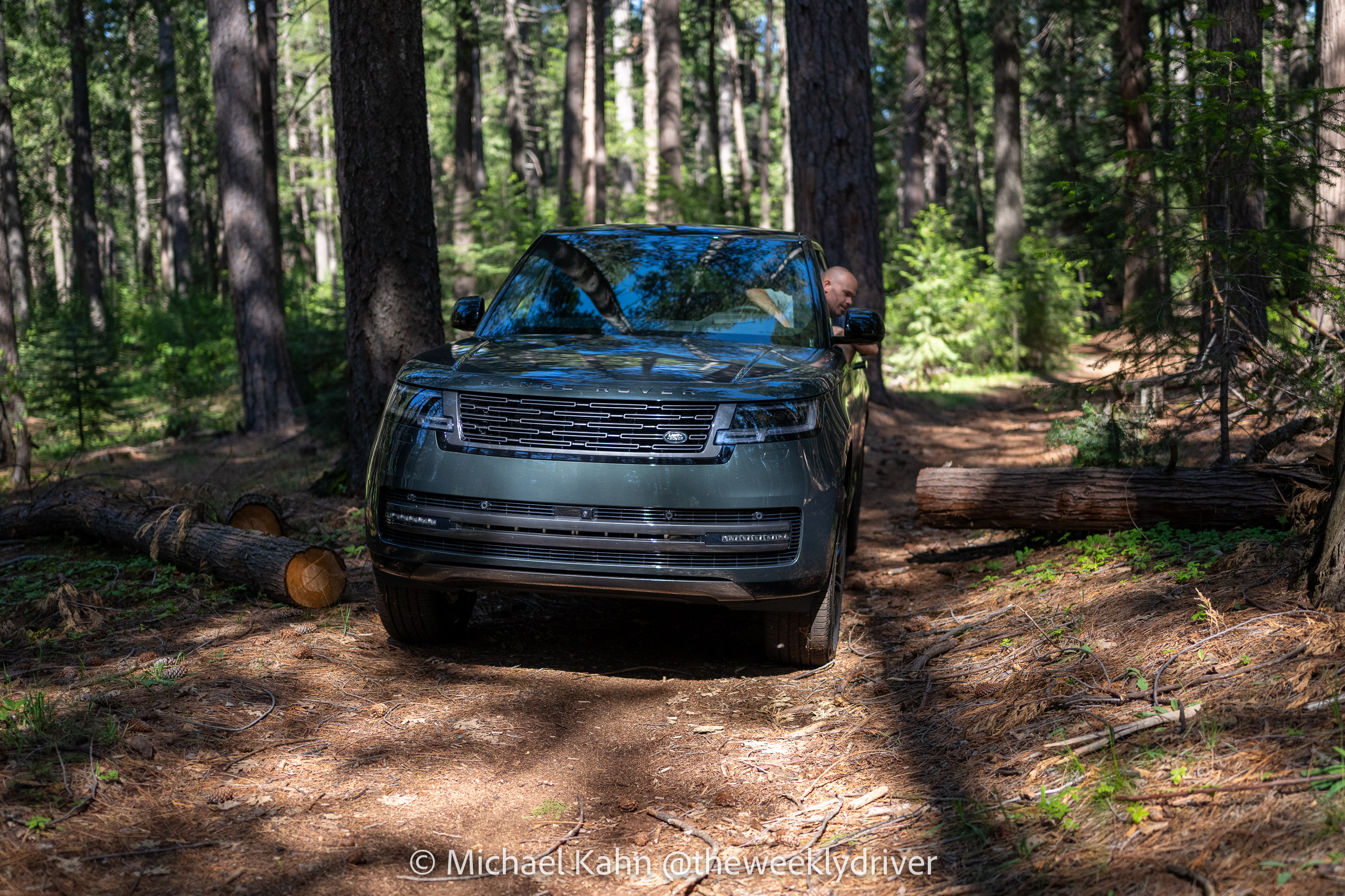 2026 Range Rover SE SWB P400 in Belgravia Green on a forest logging road, fallen logs flanking the path, driver checking positioning out the window