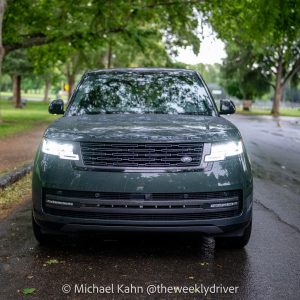 2026 Range Rover SE SWB P400 in Belgravia Green photographed head-on under a wet tree canopy, the L460 monocoque luxury SUV in the country-house setting that defines its buyer DNA