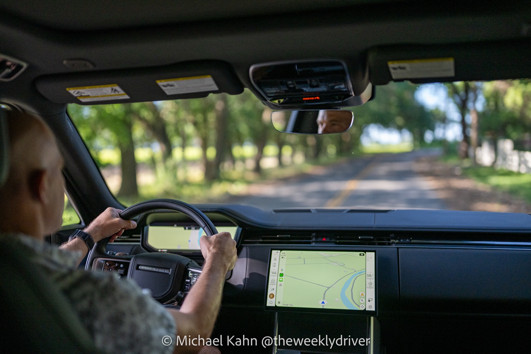 2026 Range Rover Pivi Pro center touchscreen running Google Maps via wireless smartphone projection while driving down a shaded road