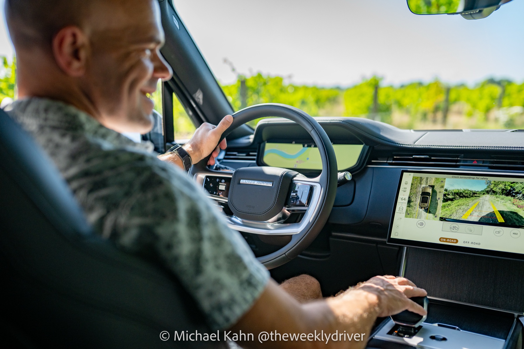 Pivi Pro 3D surround camera on-road mode displayed on the 2026 Range Rover center touchscreen with driver smiling and one hand on the wheel