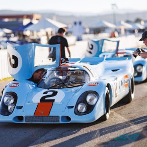 Gulf-livery Porsche 917s in the paddock at Velocity Invitational with a photographer approaching the cars without barriers