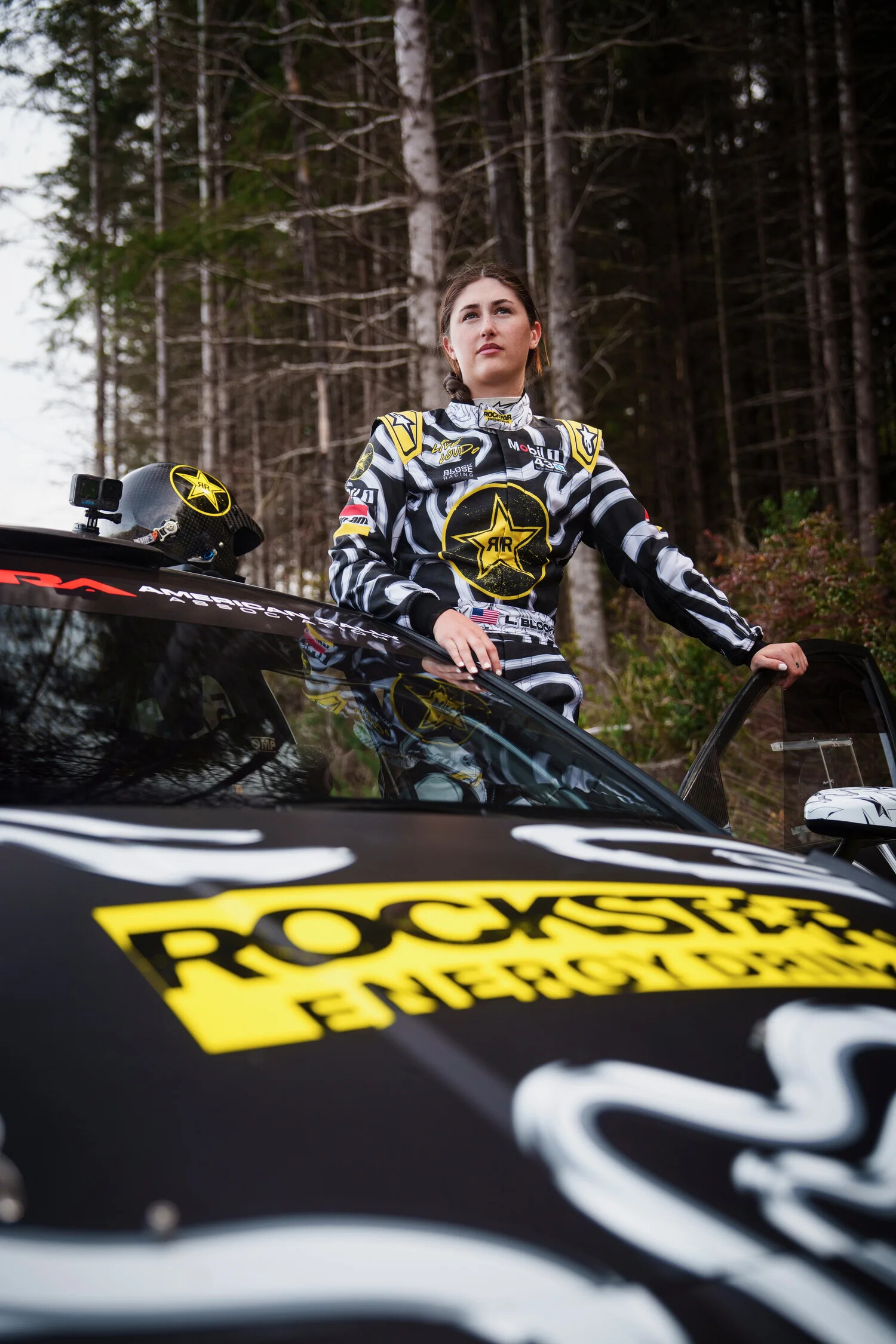Lia Block in a Rockstar Energy-livery rally suit standing beside her American Rally Association car ahead of her Sunday appearance at Velocity Invitational