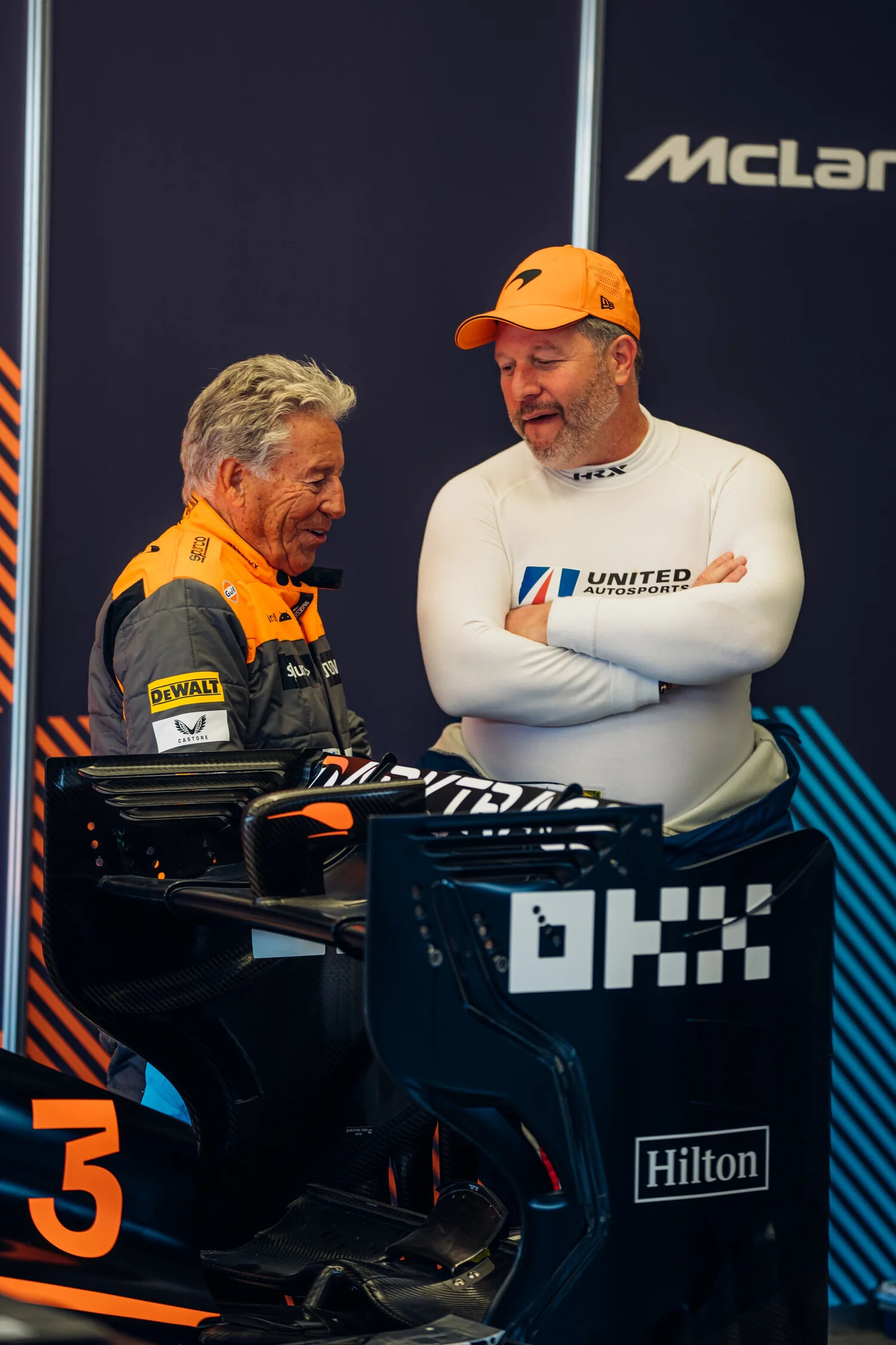 Mario Andretti in a McLaren racing suit talking with a driver in United Autosports gear inside the McLaren garage at a prior Velocity Invitational