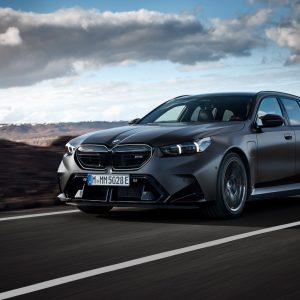 A 2026 BMW M5 Touring wagon in matte grey on a mountain road, the first M5 Touring ever sold in the United States