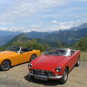 An orange MG Midget and a red MGB roadster parked at a mountain overlook in Spain