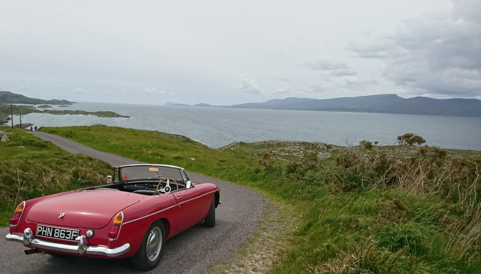 A red MGB roadster parked on a coastal road overlooking the sea in Ireland