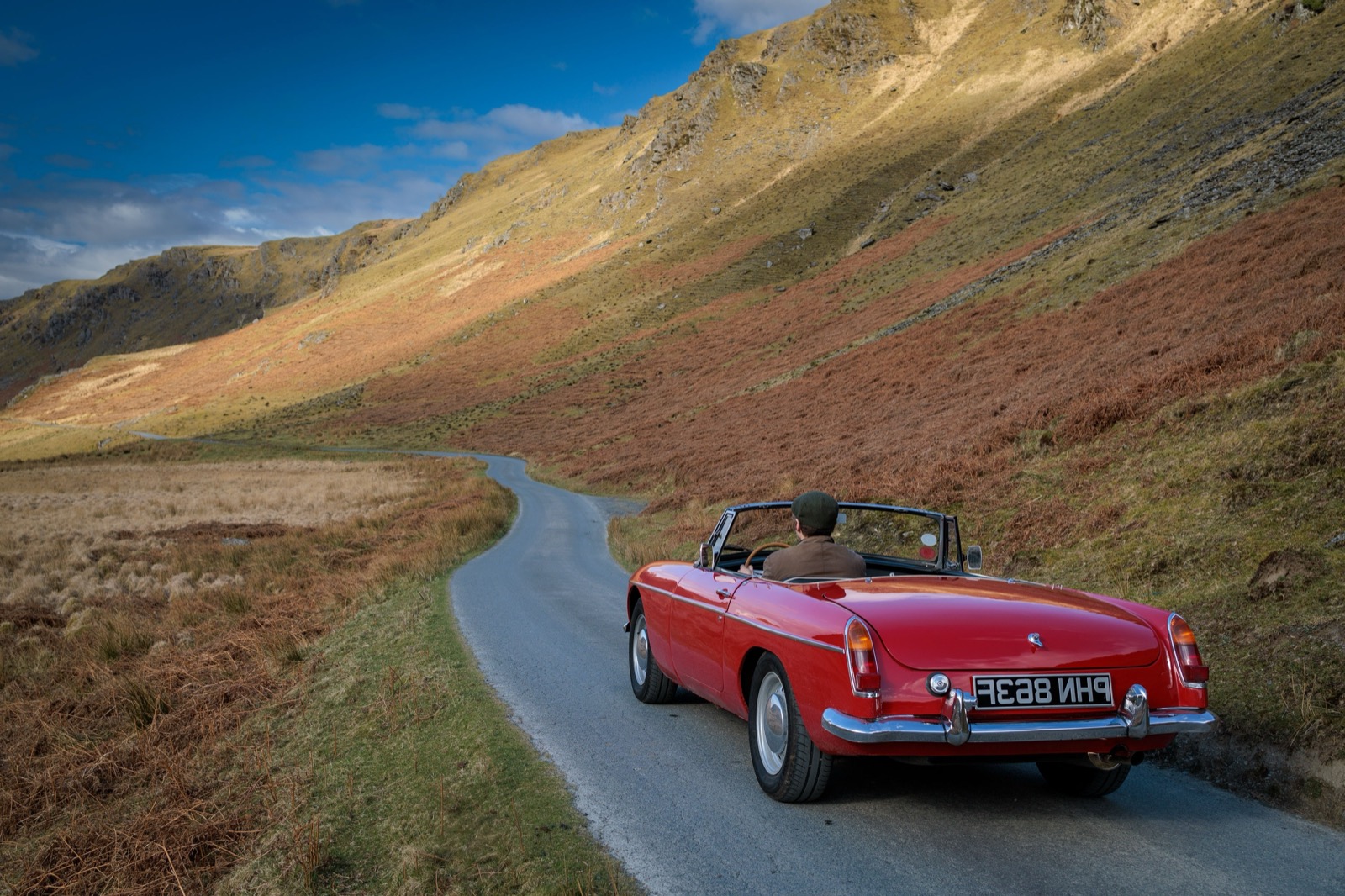 A red MGB roadster driving up a winding single-track road through the Welsh mountains