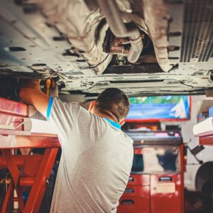A technician works beneath a vehicle on a shop lift, illustrating how direct-to-consumer automakers handle service without a dealership network