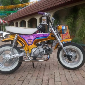 Hemmings Stay Gold one-of-one custom CT-70 Trail 70 minibike in gold metal-flake paint with candy-purple flames, side profile, the prize in the 2026 Hemmings Stay Gold Sweepstakes