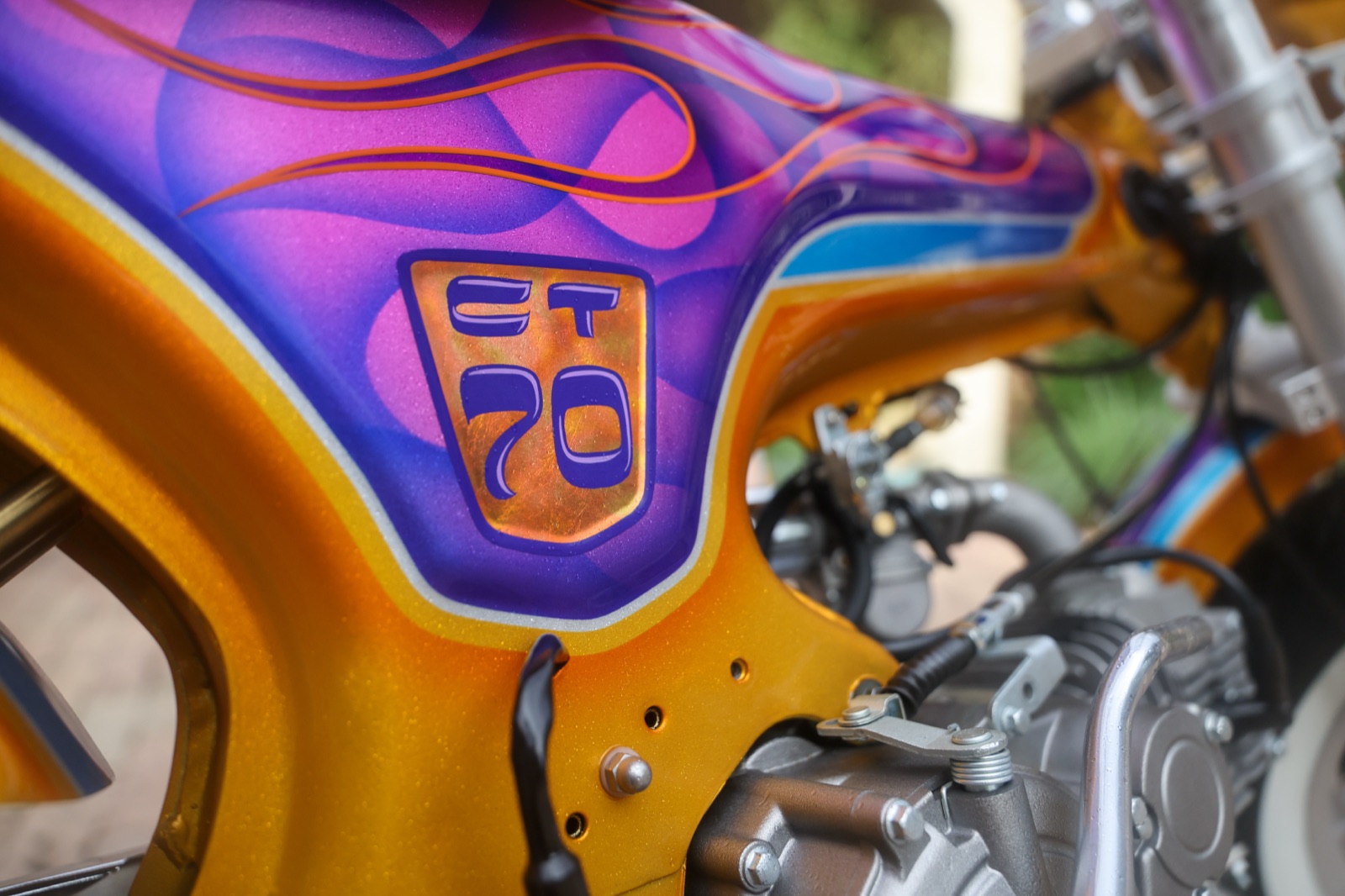 Detail of the gold metal-flake base, candy-purple flames, blue pinstriping, and CT70 shield painted by Travis Tuki Hess on the Hemmings Stay Gold minibike