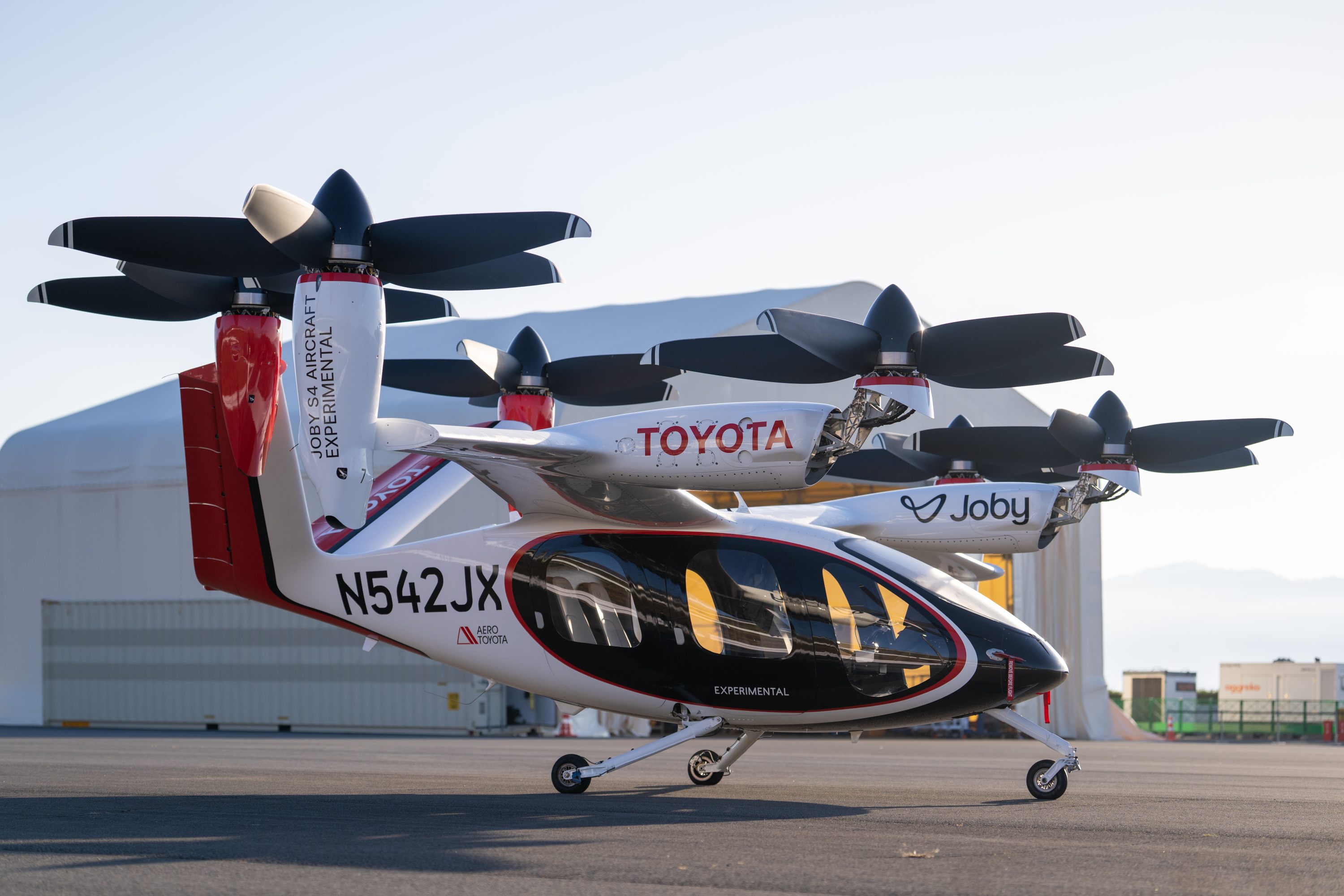 Two Joby S4 electric air taxis parked outside a hangar, one with Toyota and Aero Toyota branding and one in Joby livery, showing the six-rotor eVTOL configuration