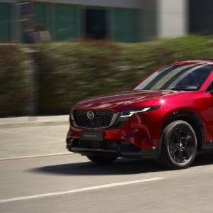 A red 2026 Mazda CX-5 driving on a city street, the redesign that earned a Top Safety Pick+