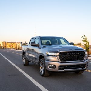 2026 RAM 1500 Express in Billet Silver Metallic driving on a road past a water tower