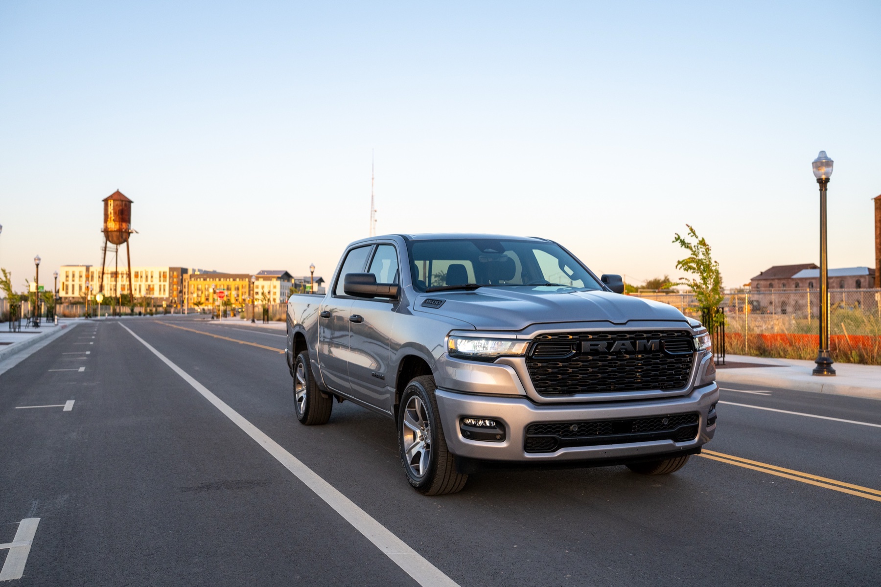 2026 RAM 1500 vs Ford F-150: The Work-Spec Truth 1 2026 RAM 1500 Express in Billet Silver Metallic driving on a road past a water tower