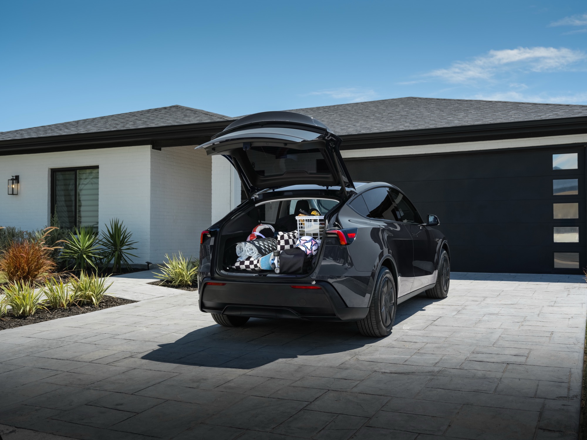 A 2026 Tesla Model Y with the rear hatch open, loaded with luggage in a driveway