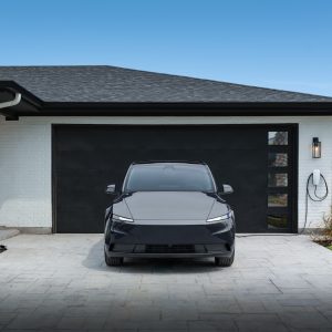 A 2026 Tesla Model Y parked in a driveway beside a wall-mounted home charger