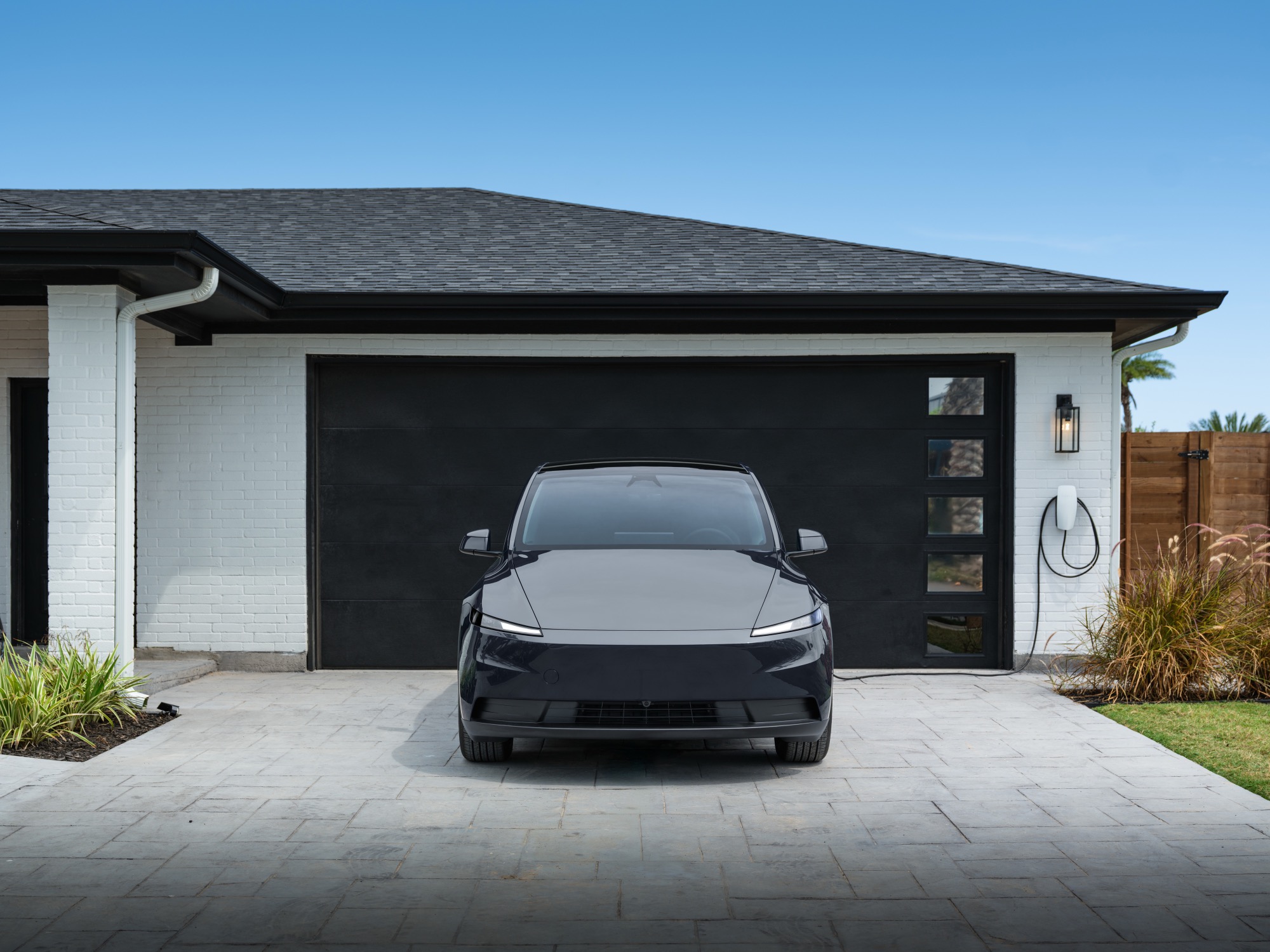 A 2026 Tesla Model Y parked in a driveway beside a wall-mounted home charger
