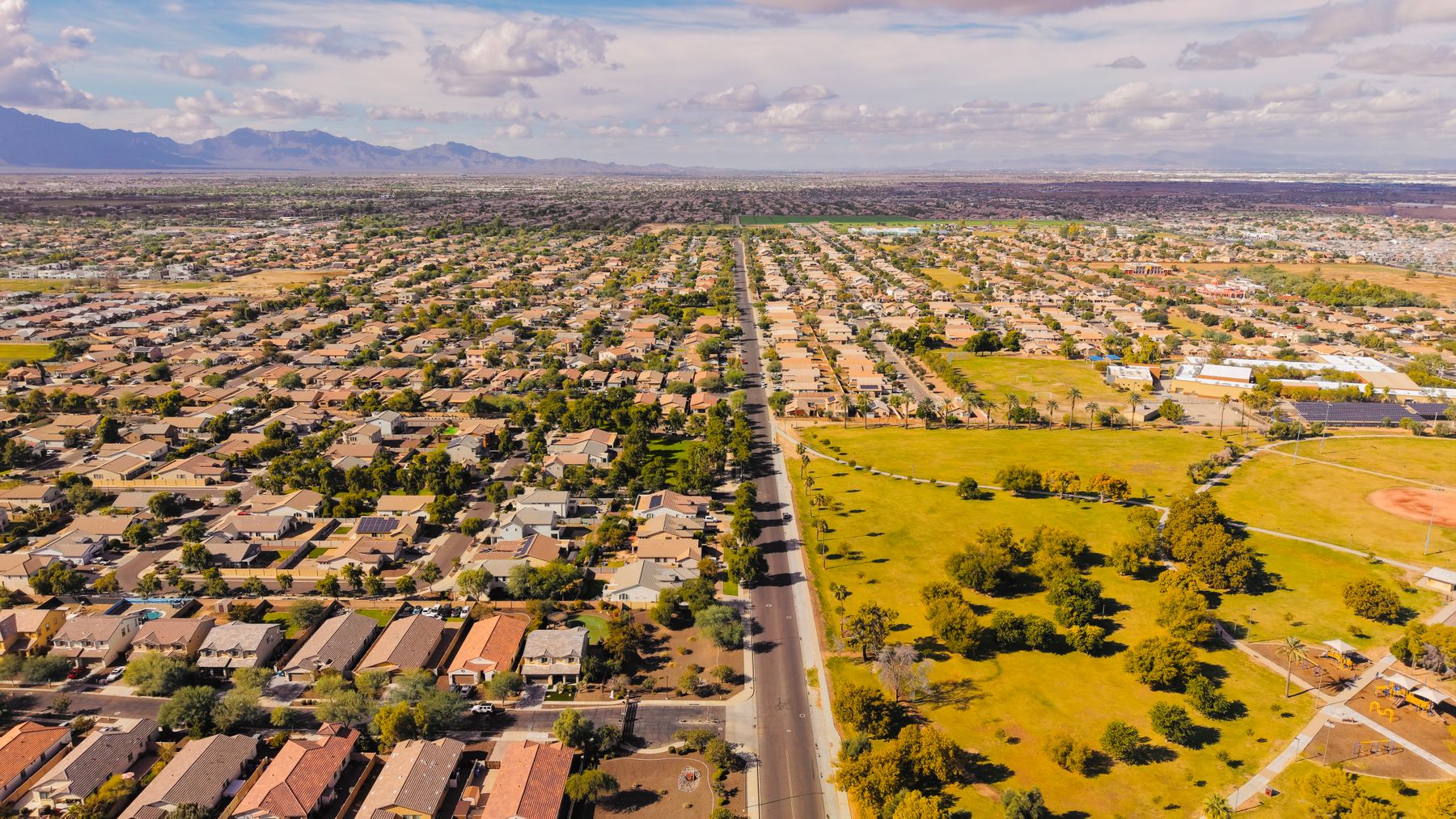 Arizona’s Fastest-Growing Suburbs Are Outrunning Their Roads — Here’s What the Crash Data Shows 1 Aerial view of a suburban Arizona arterial road running straight through dense tract housing, with a park, further subdivisions and mountains visible toward the horizon
