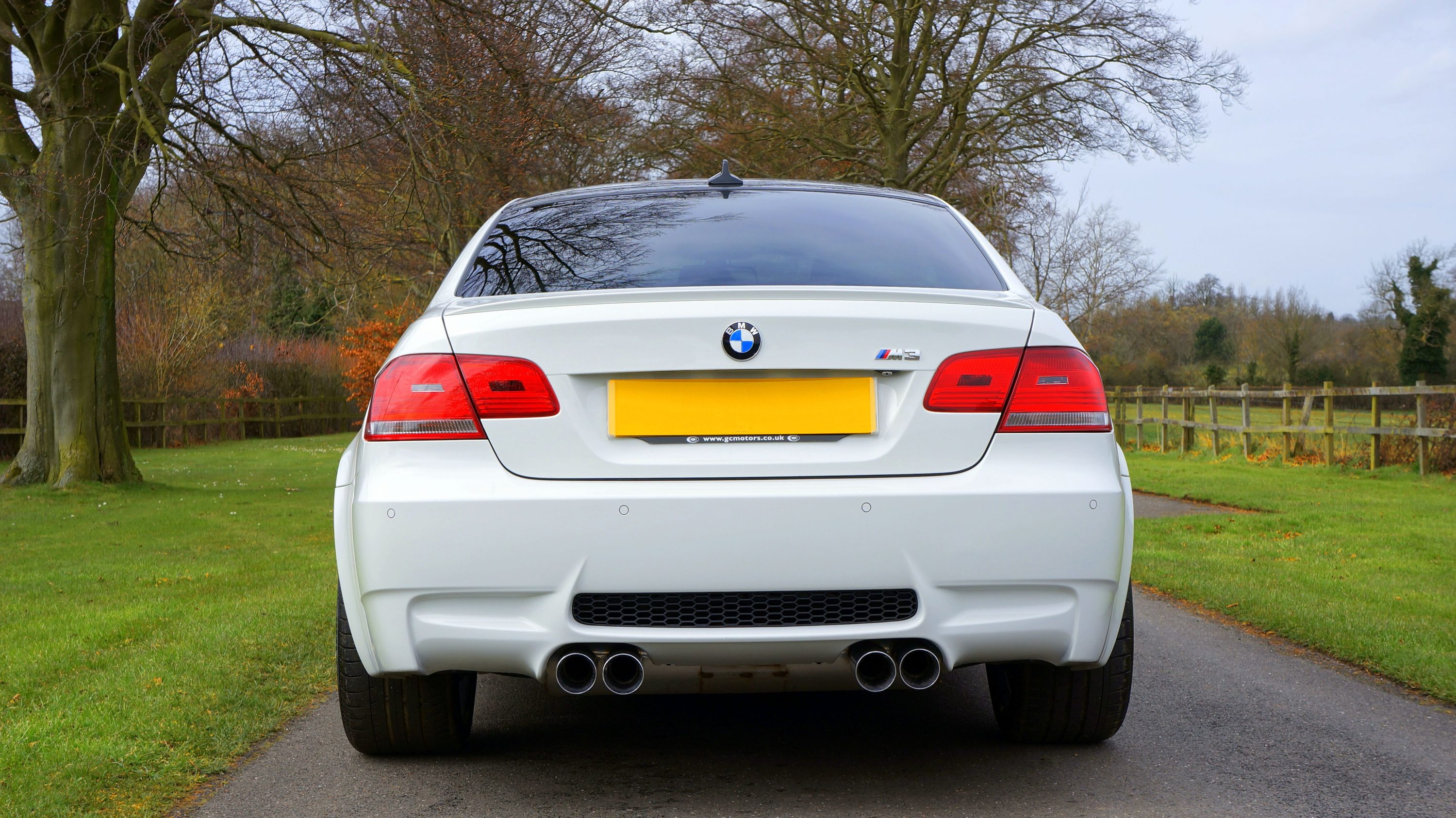 White BMW M3 parked on a countryside road, rear three-quarter view