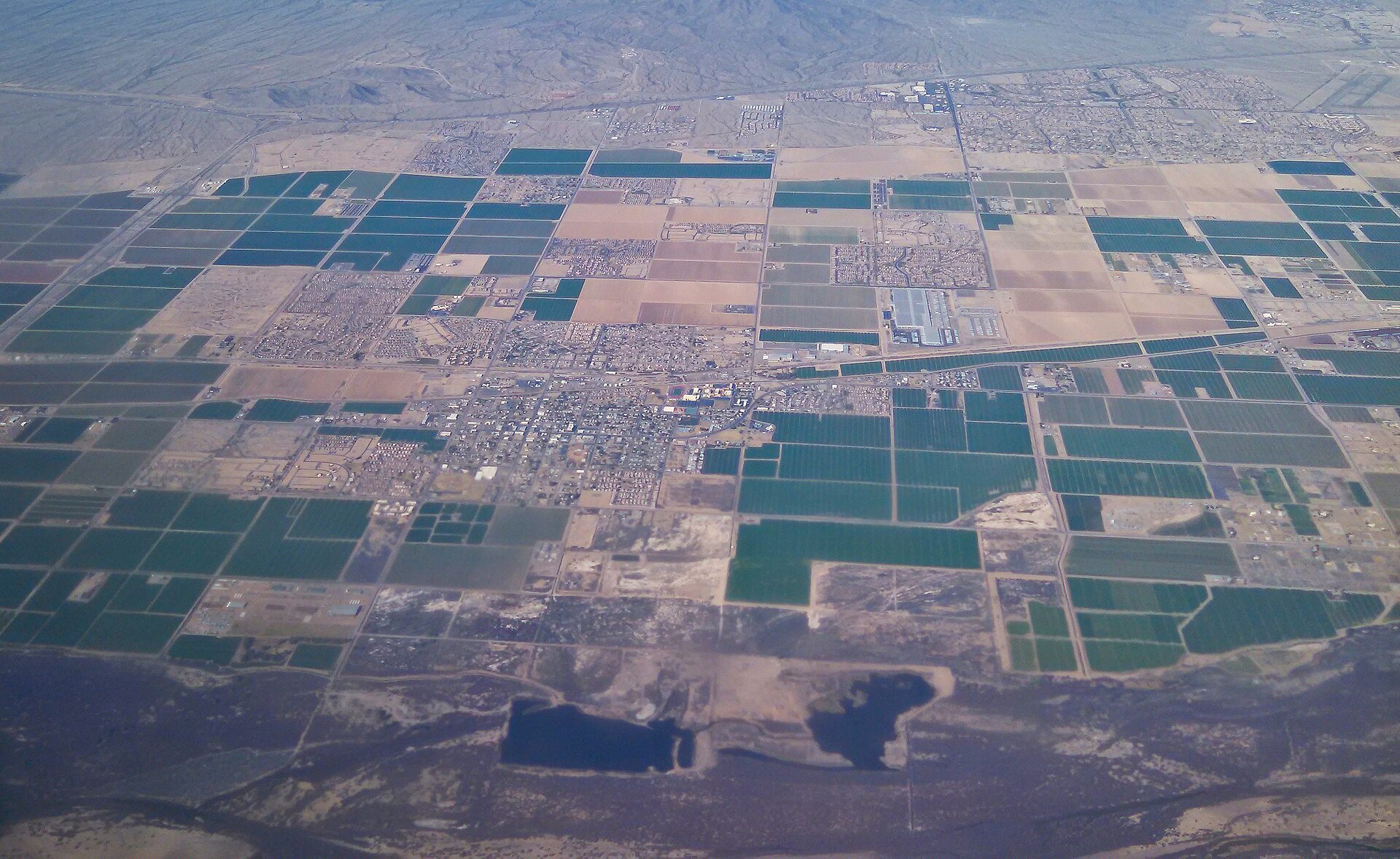 Arizona’s Fastest-Growing Suburbs Are Outrunning Their Roads — Here’s What the Crash Data Shows 8 Aerial view of Buckeye, Arizona, showing irrigated farm fields giving way to new residential subdivisions along a section-line road grid in Maricopa County's West Valley