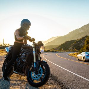 Motorcyclist stopped on the shoulder of a winding canyon road at sunset as a car passes on the curve