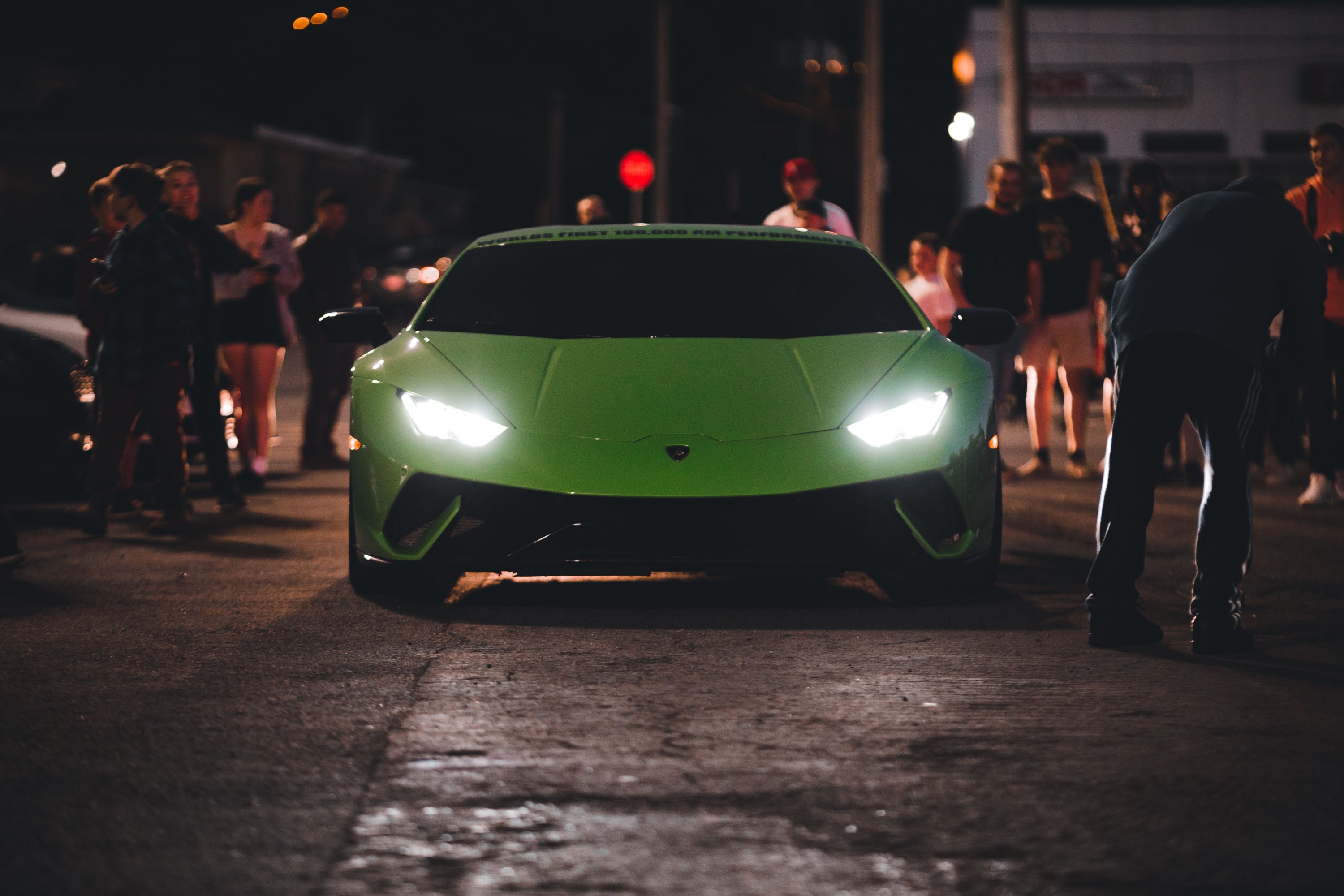 Green Lamborghini surrounded by a crowd at an evening car event