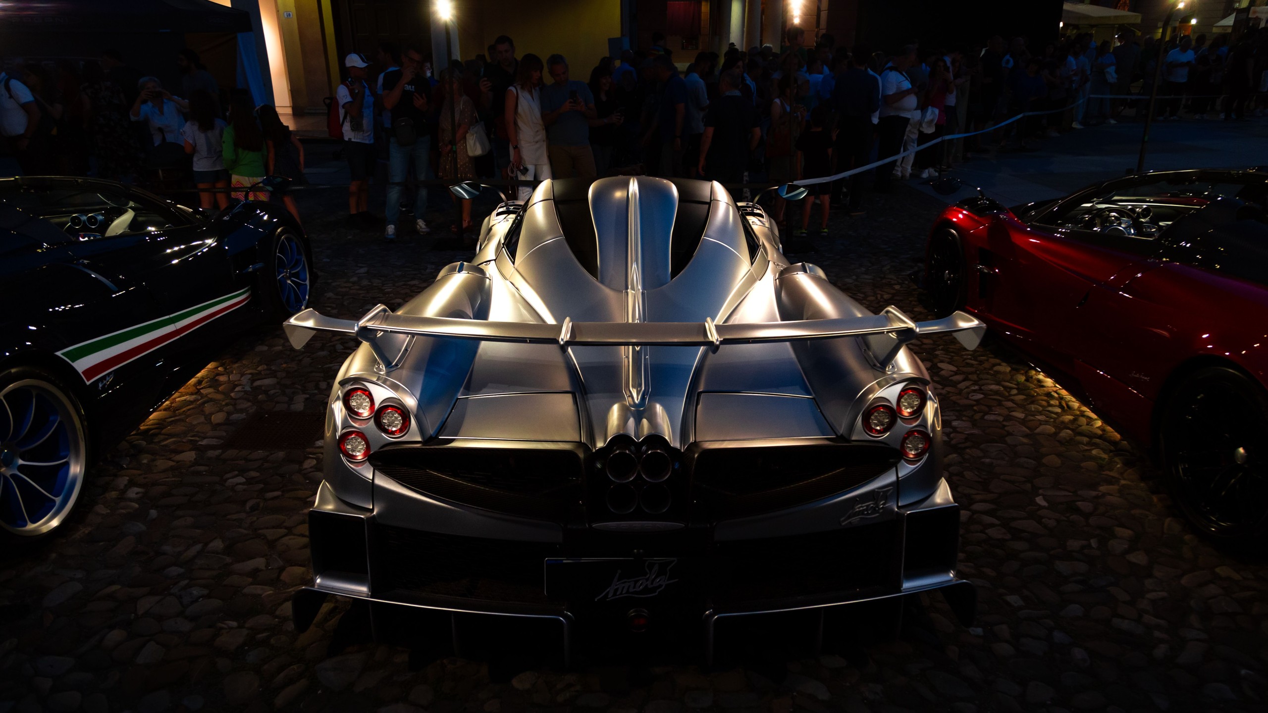 Silver supercar illuminated under lights at a night automotive exhibition