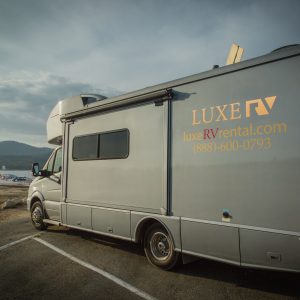 Luxury motorcoach parked on a scenic shoreline with mountains behind