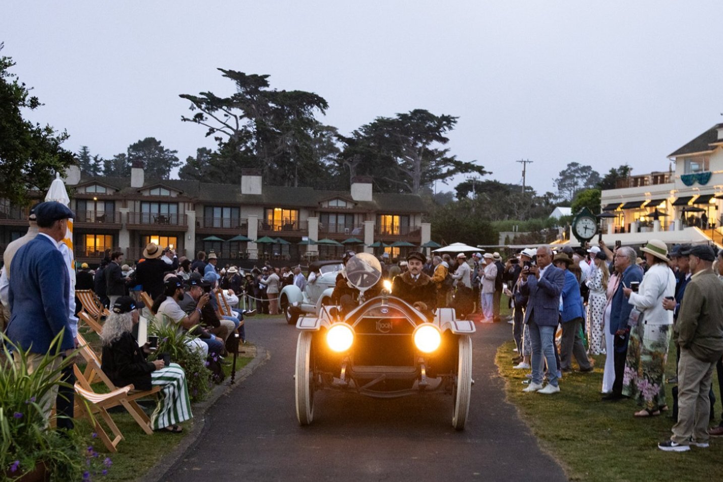 Prewar car arriving at dawn with headlights lit as spectators watch from deck chairs at Pebble Beach