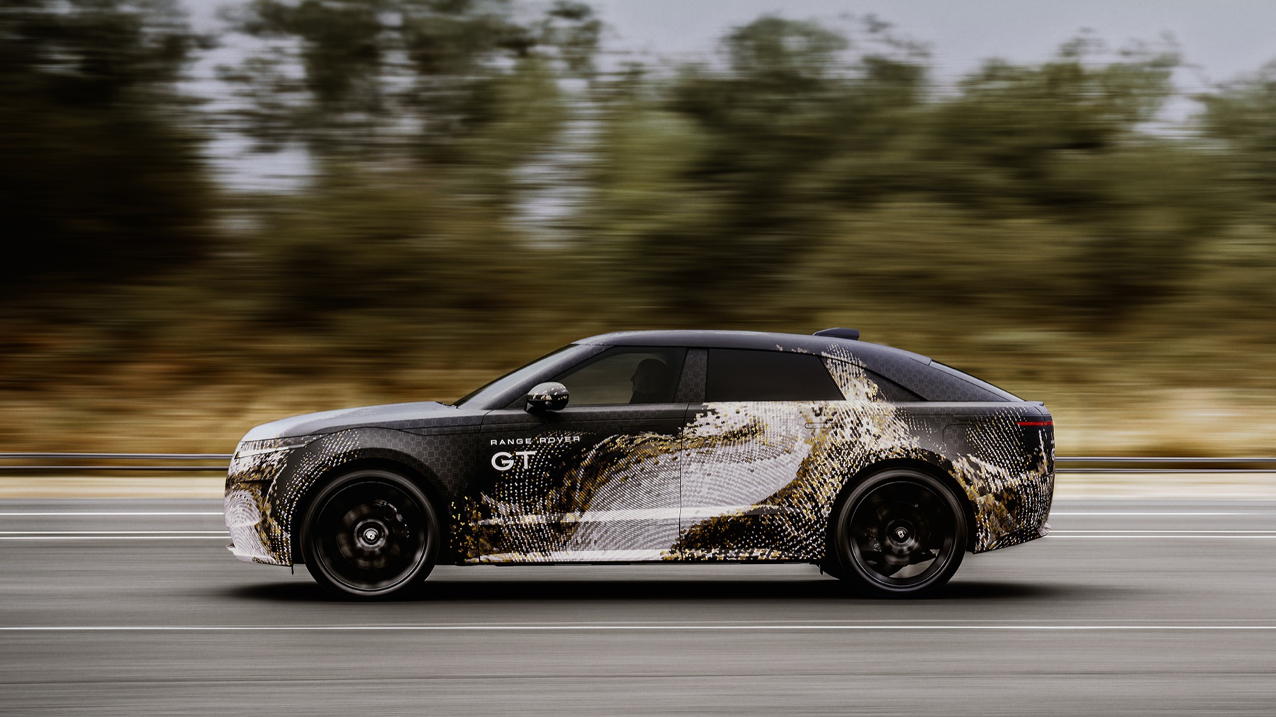 Camouflaged Range Rover GT prototype in motion, side profile showing the low roofline and fastback rear