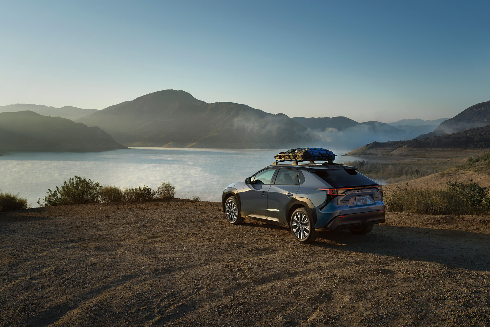 Subaru Solterra electric SUV with a roof cargo box parked above a lake at dusk