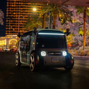 Zoox purpose-built robotaxi with roof-mounted sensor pods driving on the Las Vegas Strip at night with passengers aboard