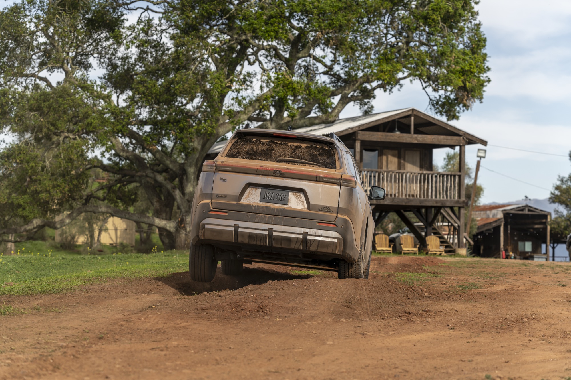 2026 Toyota bZ Woodland parked on dirt beside a rustic wooden cabin, rear three-quarter view