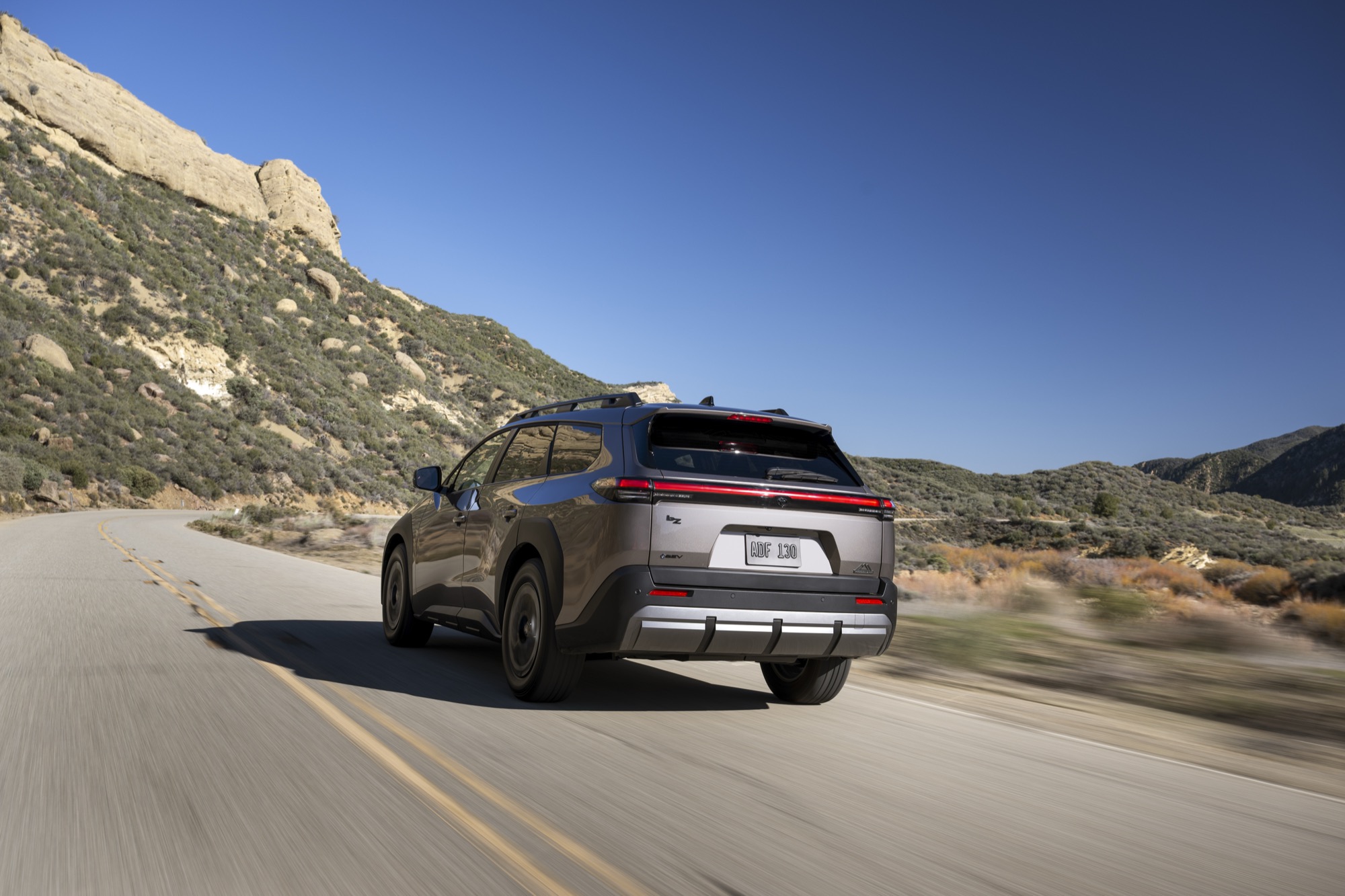 2026 Toyota bZ Woodland driving away on a mountain road, rear three-quarter view